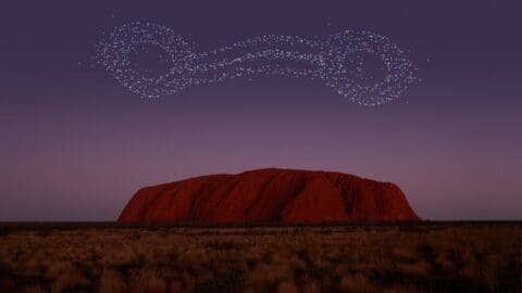 A night sky displays a cluster of small lights forming two connected circles above a large rock formation in a desert landscape, perfect for an ecotourism tour under the stars.