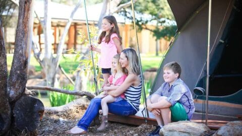 A mother with three children sit on the terrace of a tent and smile while looking in the distance.