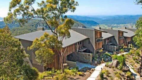 Several modern cabins set against a mountainous landscape with lush greenery and a clear sky in the background, perfect for an ecotourism getaway.