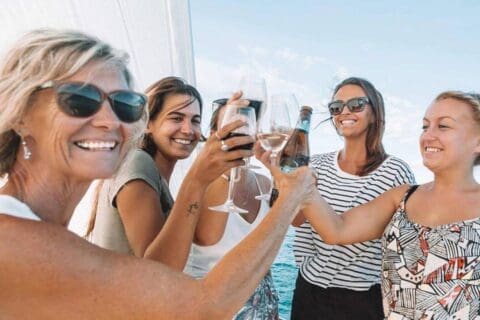 Four women toasting with wine glasses on a boat under a clear sky, celebrating their sailing adventure through the stunning Whitsundays.