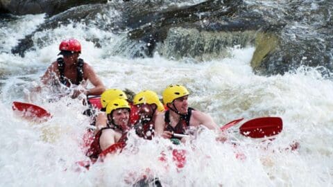 A group of adventurers wearing helmets and life jackets navigate through rough waters while whitewater rafting, immersed in the beauty of nature.