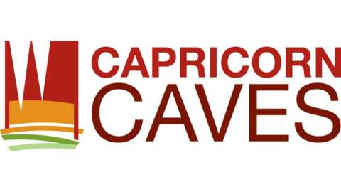 Logo of Capricorn Caves featuring stylized rock formations in red and yellow with green lines underneath, along with the text "Capricorn Caves" in bold red letters, highlighting their commitment to ecotourism.