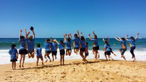 A group of people standing next to each other and jumping with their arms up on the beach.