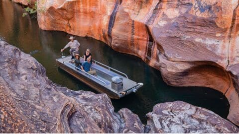 Three people ride in a small motorboat through a narrow, rocky canyon, experiencing the beauty of nature. This ecotourism adventure offers an intimate journey with picturesque views.