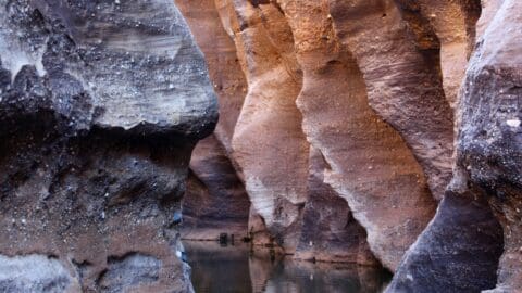 Discover the beauty of this narrow slot canyon with smooth, layered rock walls in shades of brown and orange, reflecting in a calm pool of water at the bottom. Perfect for nature enthusiasts looking for a sustainable tour experience.