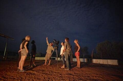 A group of people gathered around a telescope at night at the World Nature Centre, with one person pointing towards the sky.