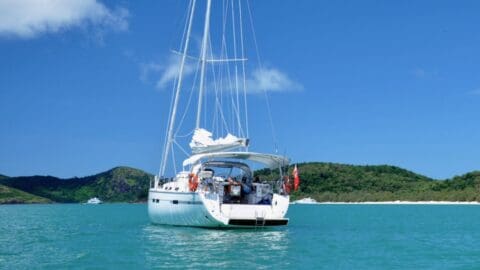 A sailboat, aptly named Curlew, is anchored on clear blue water, offering a serene escape with green hills and a blue sky gracefully framing the background.