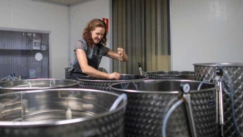 A cheerful women stirring in one of multiple shining, silver barrels.