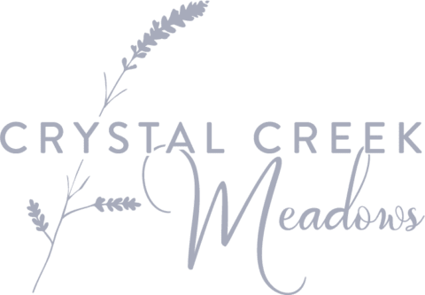 Logo of "Crystal Creek Meadows" featuring lavender sprigs intertwined with the text, highlighting sustainable accommodation in a nature-inspired design.