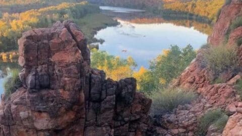 Experience the stunning view from a rocky cliff overlooking a river, encompassed by dense forest and lush vegetation, under a clear sky. Join our sustainable tour for an unforgettable adventure in nature's paradise.