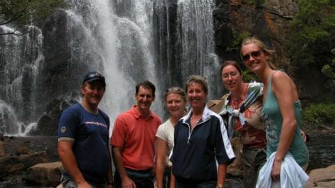 A group of six people stands in front of a stunning waterfall, enjoying a sustainable nature tour.