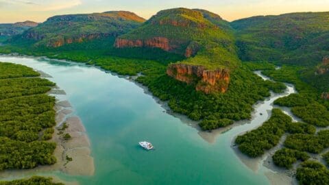 Aerial view of a river winding through lush hills with a boat on the water, surrounded by dense vegetation and rugged terrain, perfect for ecotourism enthusiasts.