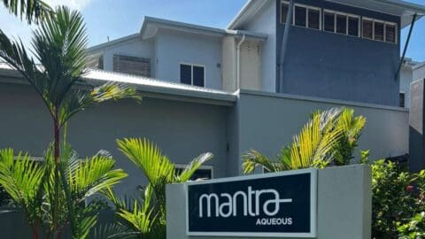 A modern, grey building with a sign in front stating "mantra Aqueous".