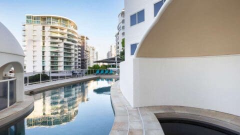 A long, quite pool surrounded by white, modern buildings.