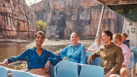 A group of people enjoys a scenic boat ride through a river canyon, with steep rocky cliffs in the background. Engaged in pleasant conversation, their inspiring journey through nature promises unforgettable memories.