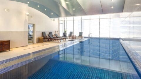 Indoor pool area with blue tiles, lounge chairs, and floor-to-ceiling windows at the Novotel Sydney Darling Square. Door at the left.