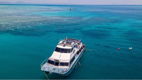 An anchored yacht next to a reef and two divers under water next to the boat.