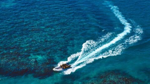 A dinghy with a group of people on it driving in clear blue water above a reef.