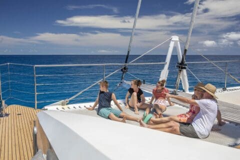 A group of people relaxes on the deck of a boat while sailing on a calm ocean under a partly cloudy sky, enjoying an ecotourism adventure.