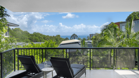A balcony with two lounge chairs and a small table at the Peppers Resort overlooks a lush green Noosa landscape and distant ocean view under a partly cloudy sky.
