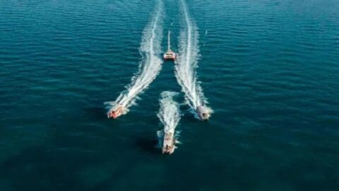 Four motorboats from Red Cat Adventures create wake trails in the ocean, viewed from above.