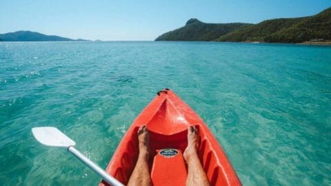 A person kayaking in clear turquoise waters with hilly islands visible in the background on a sunny day, enjoying an unforgettable ecotourism experience.