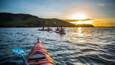 Several kayaks on a tranquil body of water at sunset, with paddlers silhouetted against rolling hills in the distance, embracing the beauty of sustainable outdoor activities.