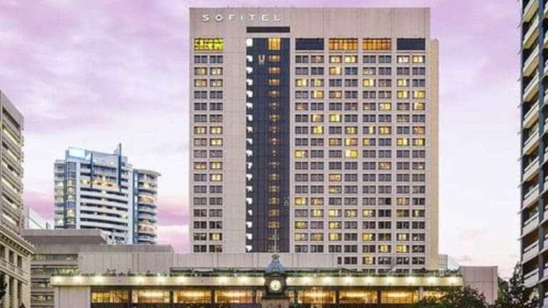 A multi-story hotel building with "Sofitel" signage at the top, surrounded by other buildings, against a backdrop of a purple sky, offering excellent accommodation for an ecotourism experience.