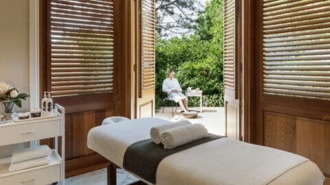 A cozy spa room with wooden walls and a woman sitting outside on the terrace drinking a cup of tea.