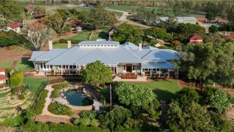 Birds view on the an estate with a large farm house surrounded by trees, a lake and other smaller buildings.