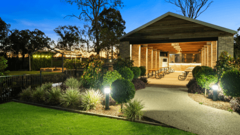 An outdoor pavilion with picnic tables and chairs is lit up at dusk, surrounded by landscaped greenery and illuminated by path lights at Splitters Farm.