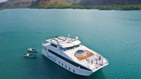 Large white yacht named "Great Escape" in calm blue waters, surrounded by scenic hills and smaller boats nearby with people on deck enjoying a nature tour.