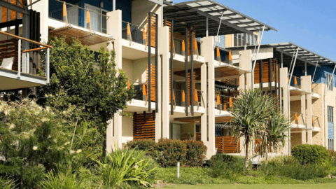 The Sebel Twin Waters boasts a three-story modern apartment building with balconies and lush greenery in the foreground under a clear blue sky.