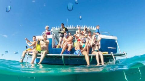 A group of people on a boat, some sitting and others standing, enjoying a sunny day on the water. Water droplets are visible on the lens, capturing a moment immersed in nature.