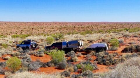 Three off-road vehicles towing trailers in a desert landscape with sparse vegetation under a clear blue sky, showcasing the beauty of sustainable ecotourism.