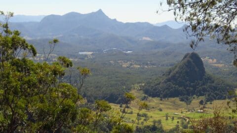 A scenic view of a mountainous landscape with lush valleys, trees in the foreground, and clear skies highlights the beauty of nature.