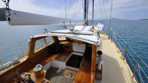 Experience the view from the deck of a sailboat at sea, showcasing seating areas, a steering wheel, and sailing equipment under a clear sky. Immerse yourself in this ecotourism adventure and connect with nature while enjoying sustainable travel on the open waters.
