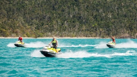 Three people riding jet skis on a turquoise body of water with a forested shoreline in the background, enjoying a sustainable adventure in nature.